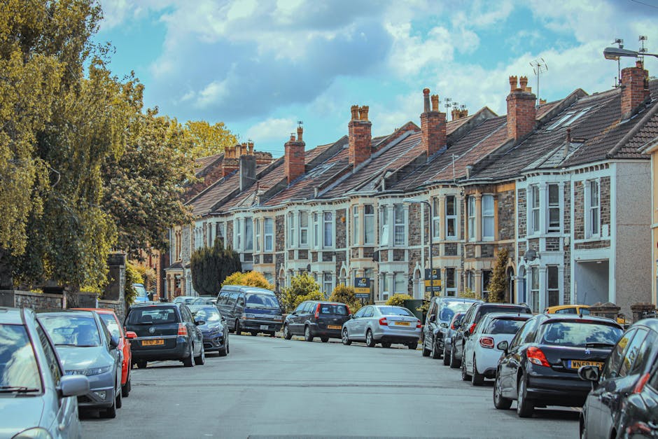 The image shows the front exterior of a two-storey terraced house with a red brick façade and a grey slate roof, situated in a residential street. The house features two ground-floor windows with whi